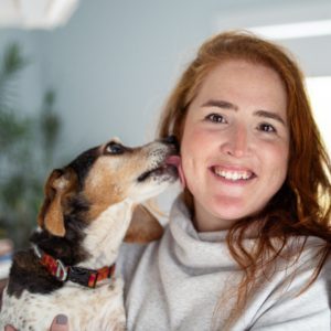 Amanda smiling with a beagle mix dog licking her cheek